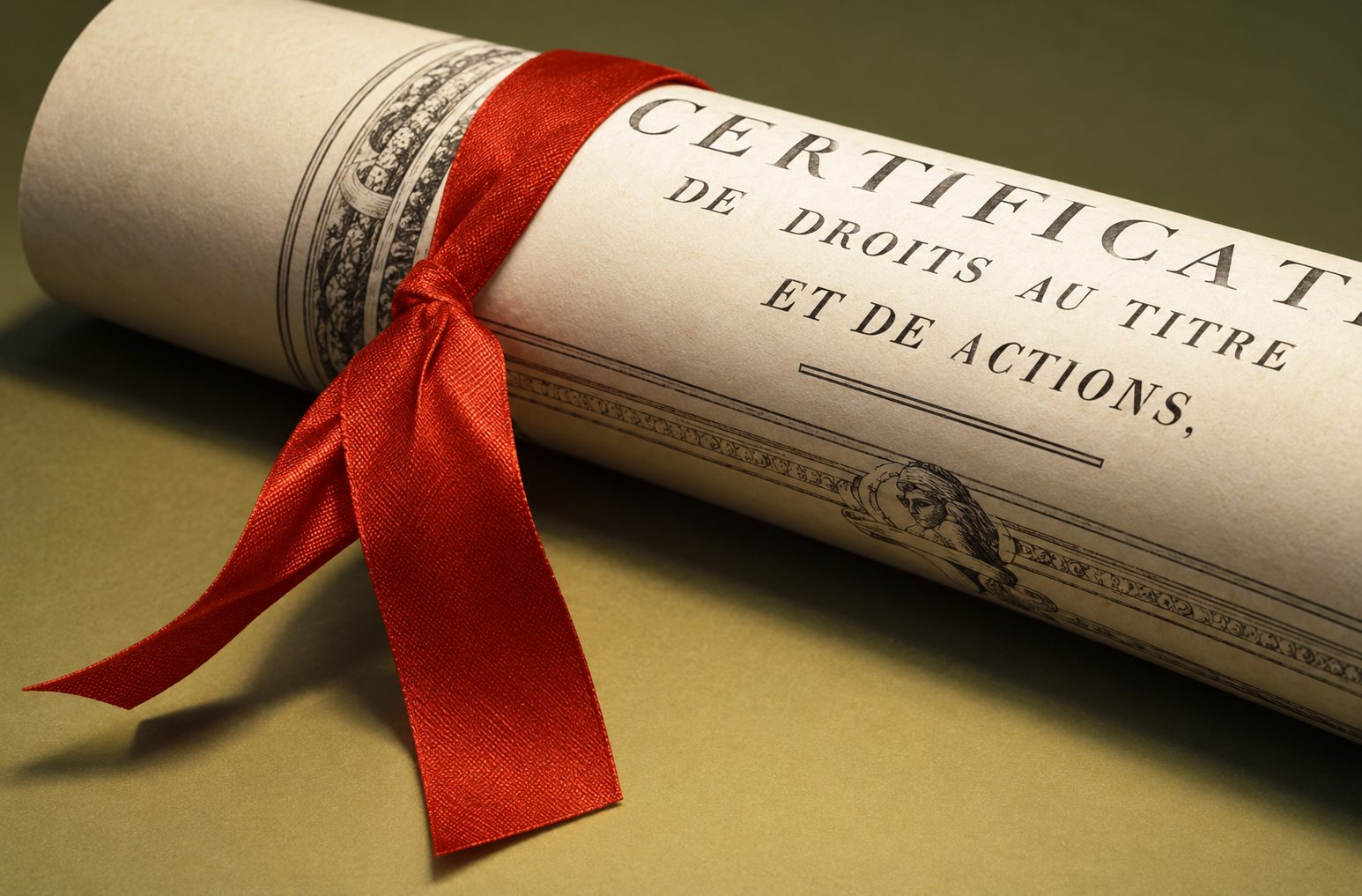 Un parchemin roulé et attaché par un ruban rouge, posé sur une surface beige.